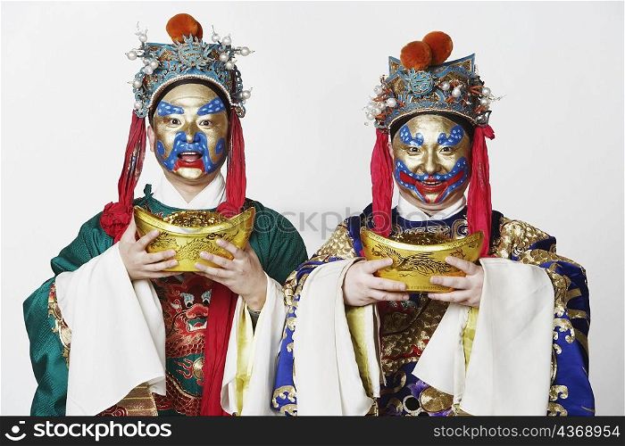 Portrait of two male Chinese opera performers holding bowls full of gold coins