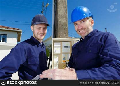 portrait of two male electricians stood by telegraph pole
