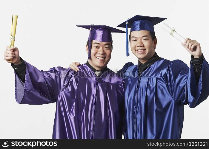 Portrait of two male graduates holding diplomas