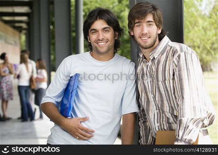 Portrait of two male university students standing in a corridor and smiling