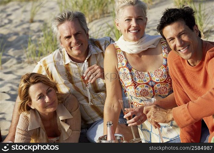Portrait of two mature couples sitting on the beach and holding champagne flutes