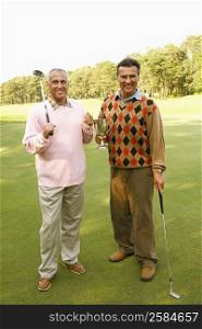 Portrait of two mature men holding a trophy and golf clubs