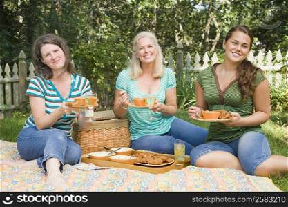 Portrait of two mature women and a young woman having picnic in a park