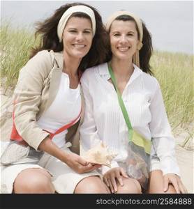 Portrait of two mature women holding a conch shell on the beach and smiling