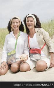 Portrait of two mature women holding a conch shell on the beach and smiling