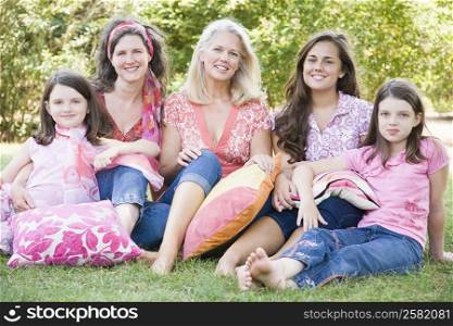 Portrait of two mature women sitting in a park with their daughters and smiling