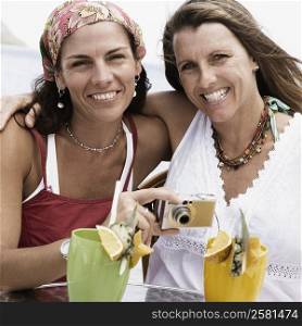 Portrait of two mid adult women holding a digital camera and smiling
