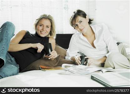 Portrait of two mid adult women holding cups of coffee on the bed