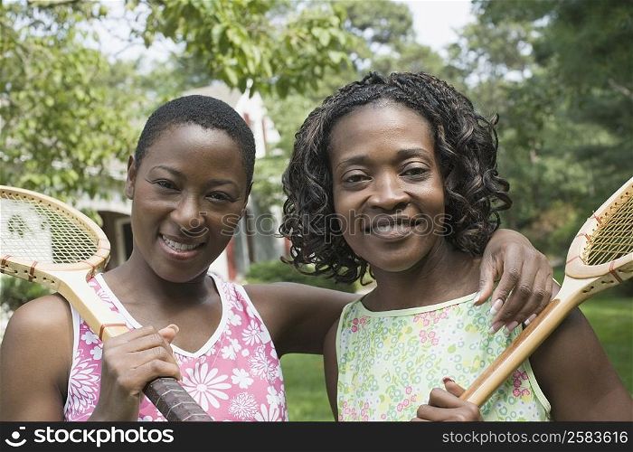 Portrait of two mid adult women holding tennis rackets and smiling