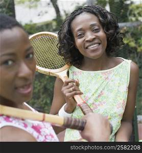 Portrait of two mid adult women holding tennis rackets and smiling in a court