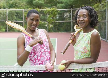 Portrait of two mid adult women holding tennis rackets and smiling in a court