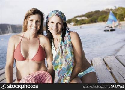 Portrait of two mid adult women sitting on a pier and smiling