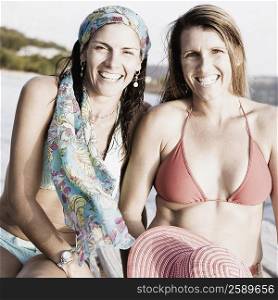 Portrait of two mid adult women sitting on a pier and smiling