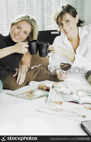 Portrait of two mid adult women toasting cups of coffee and smiling