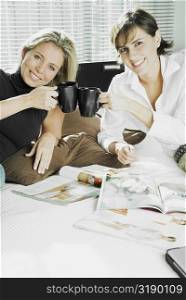 Portrait of two mid adult women toasting cups of coffee and smiling