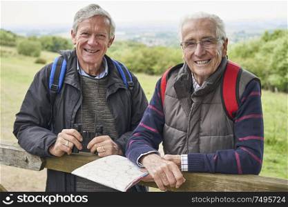 Portrait Of Two Retired Male Friends On Walking Holiday Resting On Gate With Map