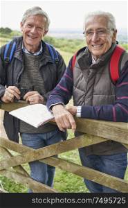 Portrait Of Two Retired Male Friends On Walking Holiday Resting On Gate With Map