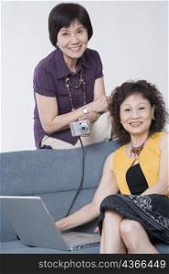 Portrait of two senior women sitting with a digital camera connected to a laptop