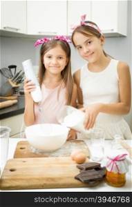 Portrait of two sister mixing ingredients for dough in big bowl on kitchen