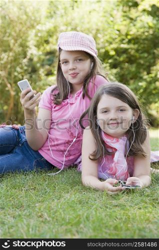 Portrait of two sisters listening to MP3 players in a park