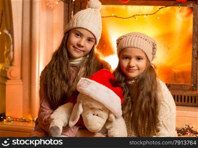 Portrait of two smiling girls sitting next to fireplace and playing with toy sheep