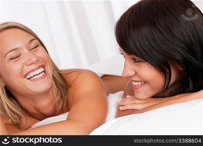 Portrait of two smiling women lying down in white bed having fun