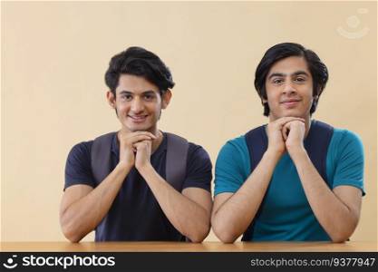 Portrait of two teenage boys looking at camera with hand on chin against plain background 