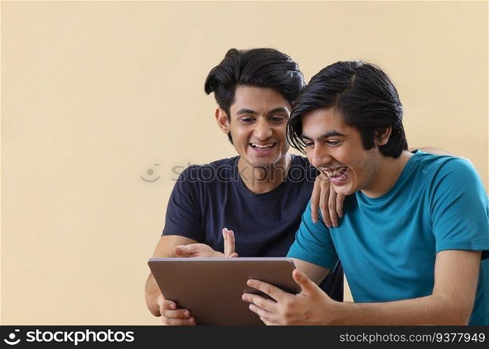 Portrait of two teenage boys using digital tablet against plain background 
