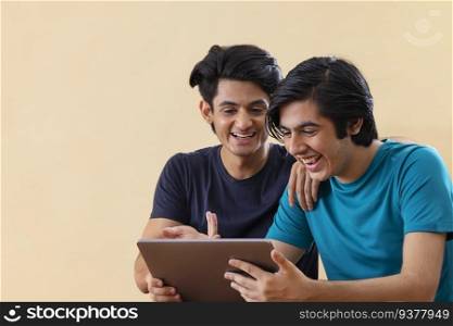 Portrait of two teenage boys using digital tablet against plain background 