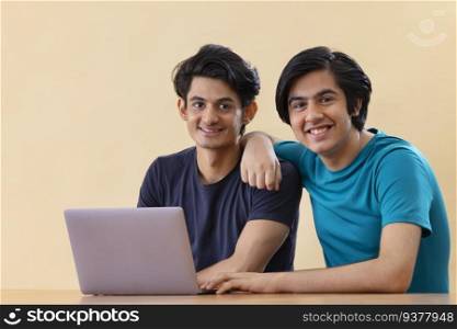 Portrait of two teenage boys using laptop against plain background 