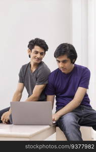 Portrait of two teenage boys using laptop against plain background 