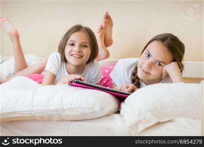 Portrait of two teenage girls lying in bed with digital tablet