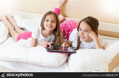 Portrait of two teenage sisters using tablet on bed at morning