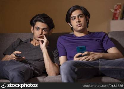 Portrait of two teenagers using smartphones while leaning on sofa in living room
