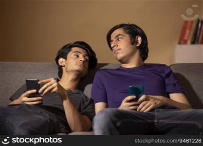 Portrait of two teenagers using smartphones while leaning on sofa in living room