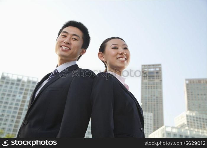 Portrait of two young business people outside in the business district, Beijing, low angle view