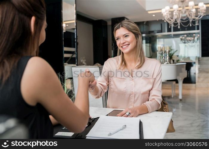 Portrait of two young businesswomen having meeting and shaking hands at hotel lobby. Business travel concept.