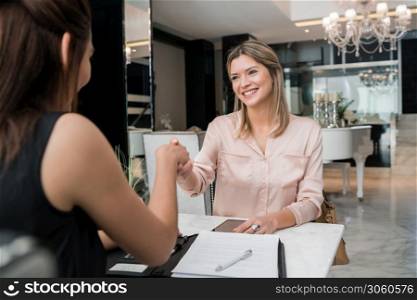 Portrait of two young businesswomen having meeting and shaking hands at hotel lobby. Business travel concept.