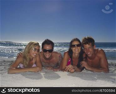 Portrait of two young couples lying down on the beach