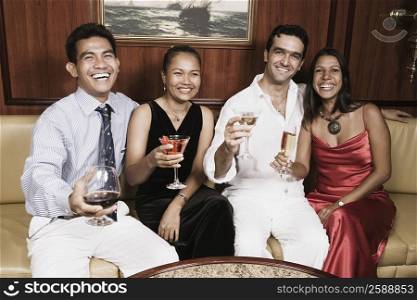 Portrait of two young couples sitting on a couch with holding their glasses and smiling