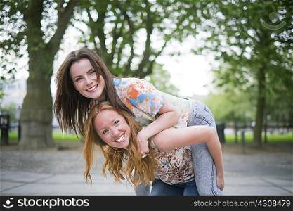 Portrait of two young female best friends giving piggy back in park