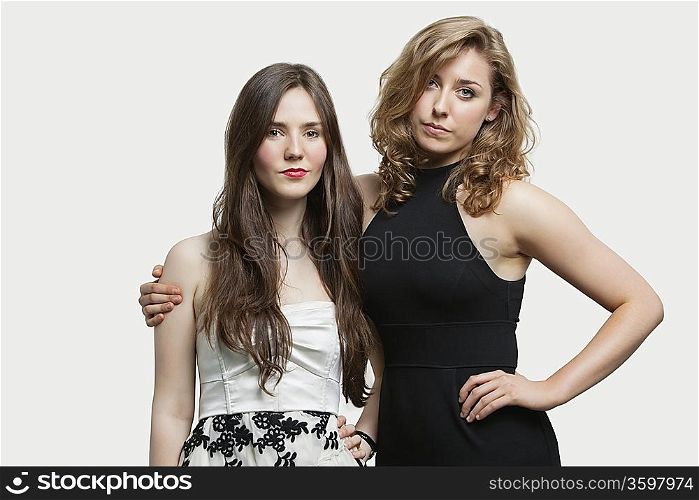 Portrait of two young female friends standing together over gray background