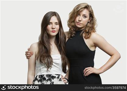 Portrait of two young female friends standing together over gray background