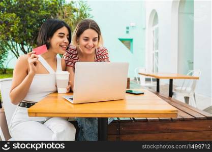 Portrait of two young friends doing online shopping with laptop and credit card at coffee shop. Shop online concept.