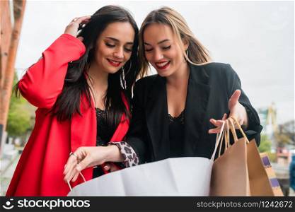 Portrait of two young friends enjoying doing shopping together while walking at the street. Friendship and shopping concept.