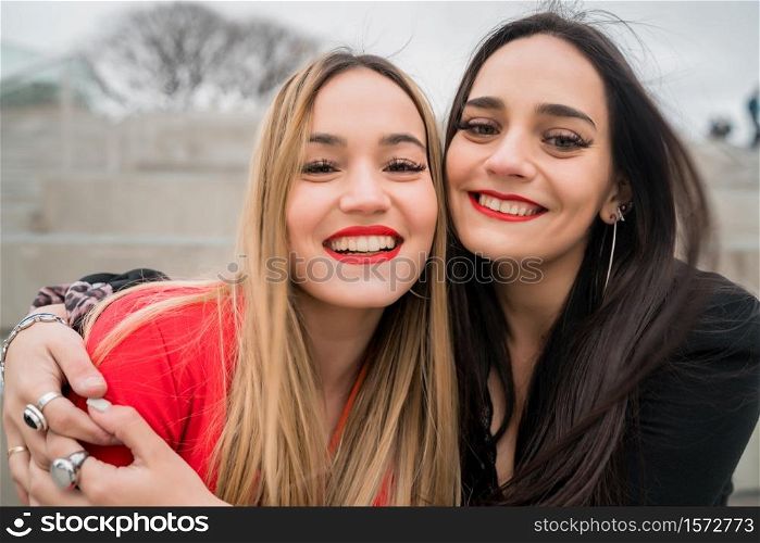 Portrait of two young friends hugging each other outdoors at the street. Lifestyle and friendship concept.