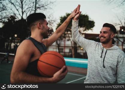 Portrait of two young friends playing basketball and having fun on court outdoors. Sport concept.