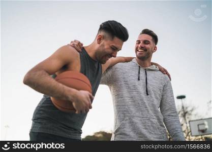 Portrait of two young friends playing basketball and having fun on court outdoors. Sport concept.