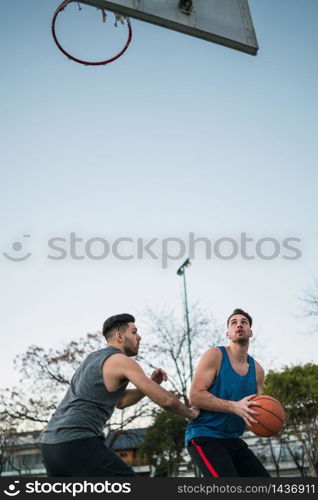 Portrait of two young friends playing basketball and having fun on court outdoors. Sports concept.