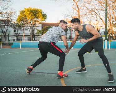 Portrait of two young friends playing basketball and having fun on court outdoors. Sports concept.